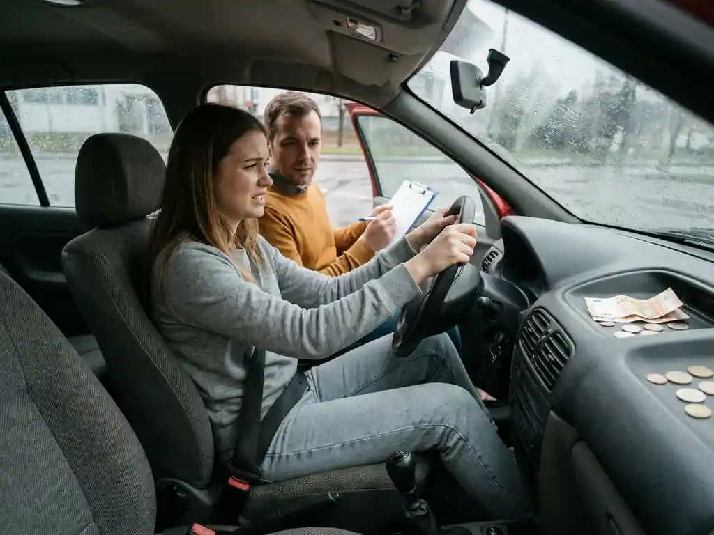 Gespannen rijschoolstudent achter het stuur met instructeur en euro's op het dashboard, gefotografeerd vanuit de passagiersstoel.